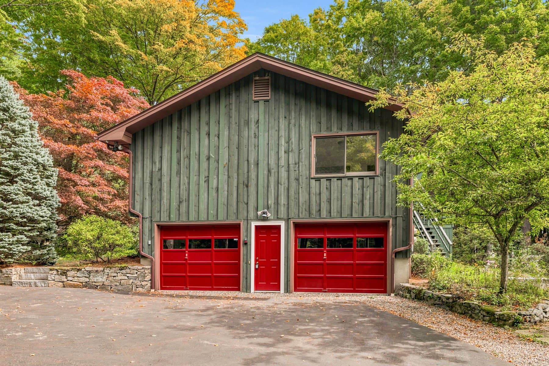 The front of the house from the driveway: green board-and-batten siding, 2 red garage doors, and a red entry door between them