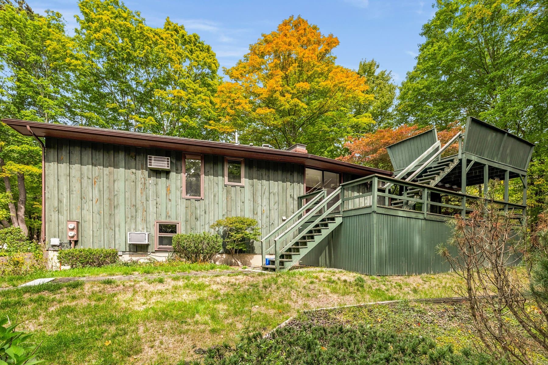The house from the side lawn, with the deck and its stairs at the back and the maples turning above