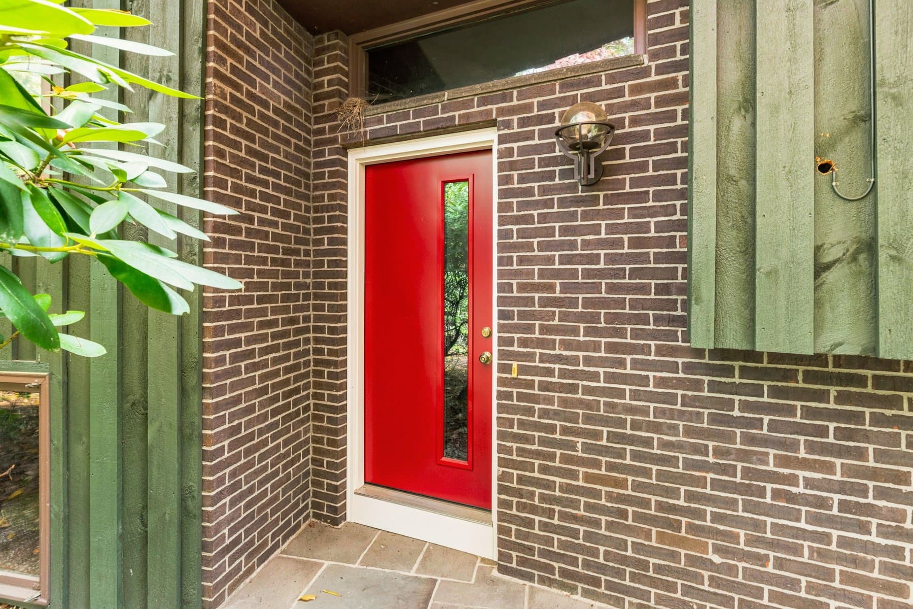 The red front door with a glass panel, set in the brick entry wall under the slate stoop
