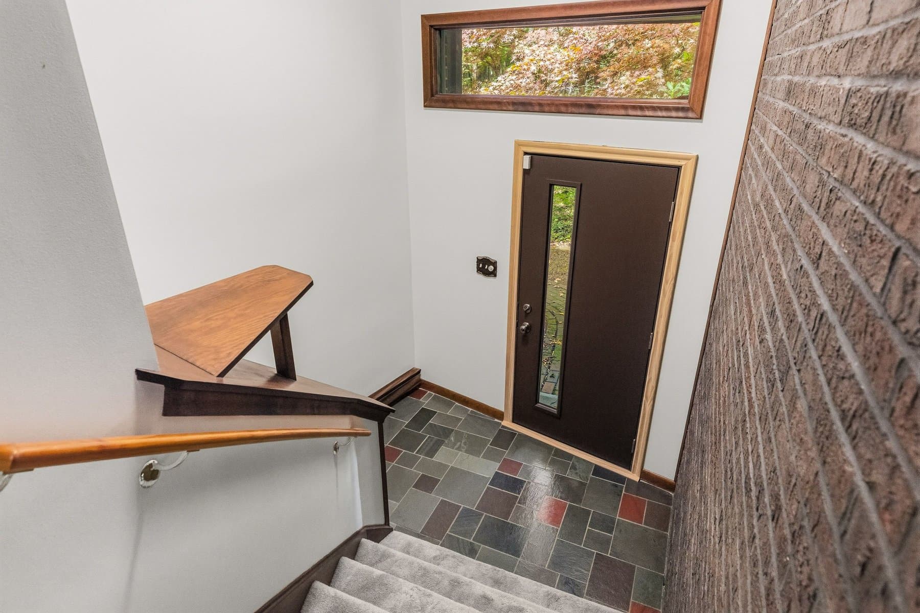 The slate-floored foyer with the front door, a brick wall, and the open stair with its wood rail
