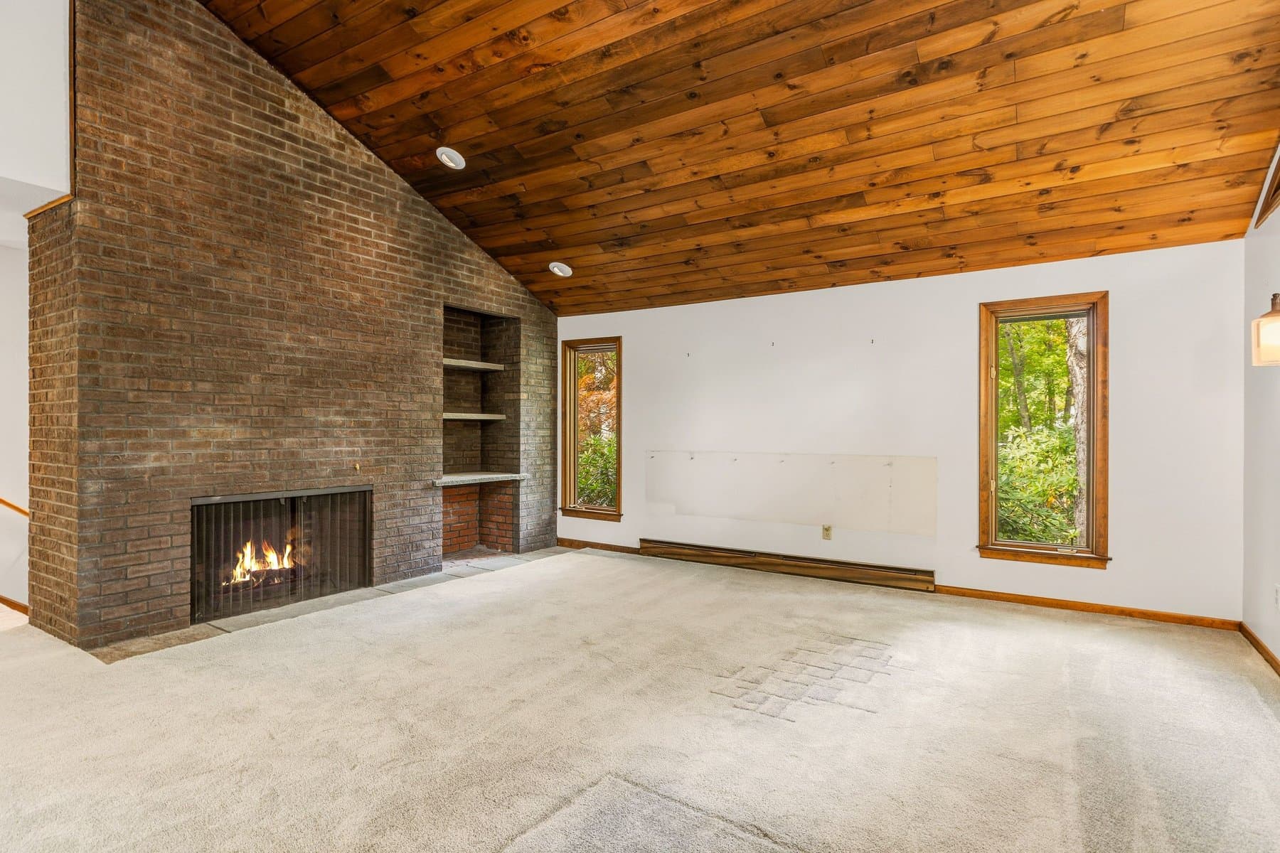 The floor-to-ceiling brick fireplace wall with built-in shelves, the fire lit