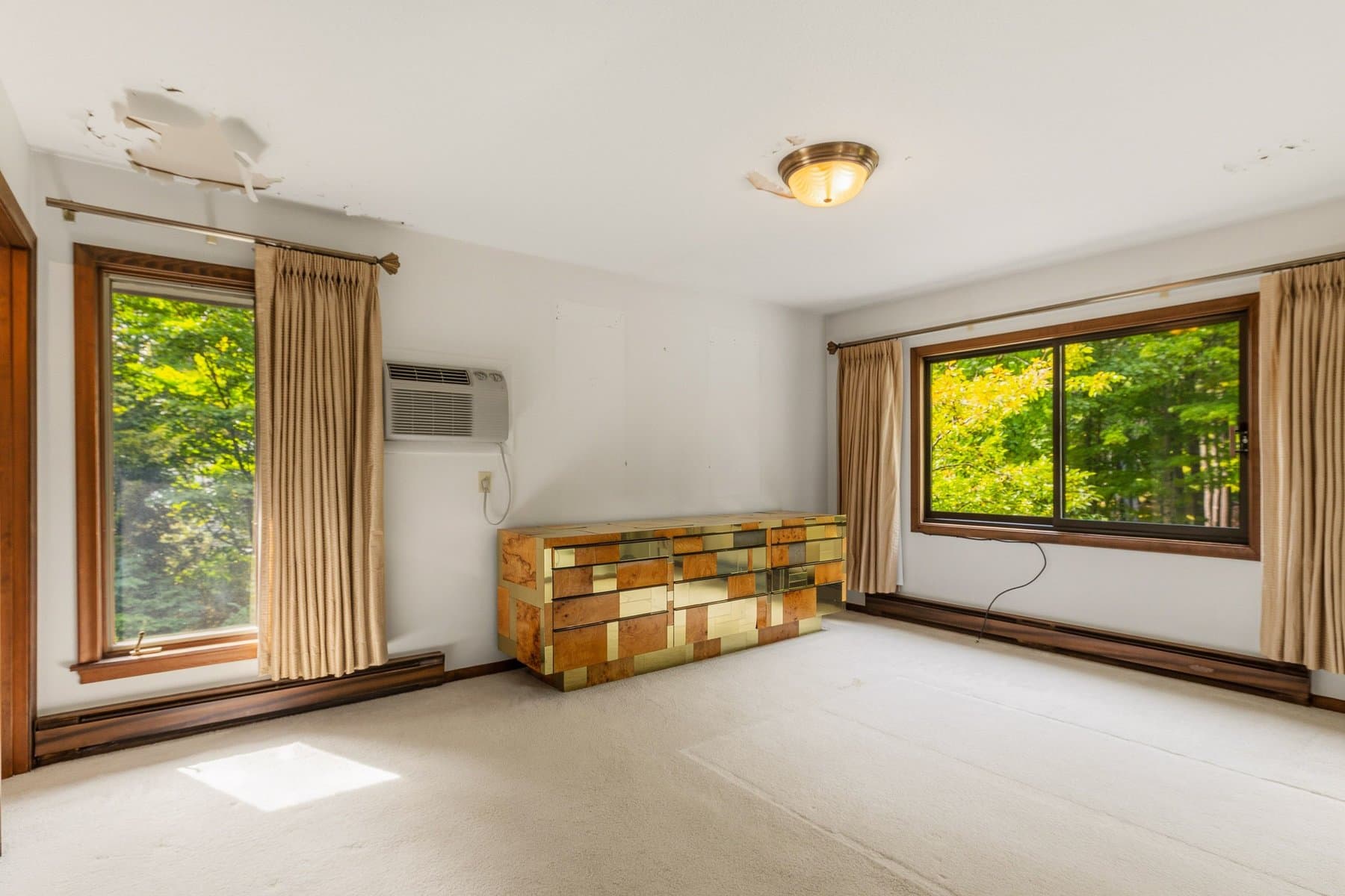 The primary bedroom with 2 windows, a window air conditioner, and a patchwork wood dresser