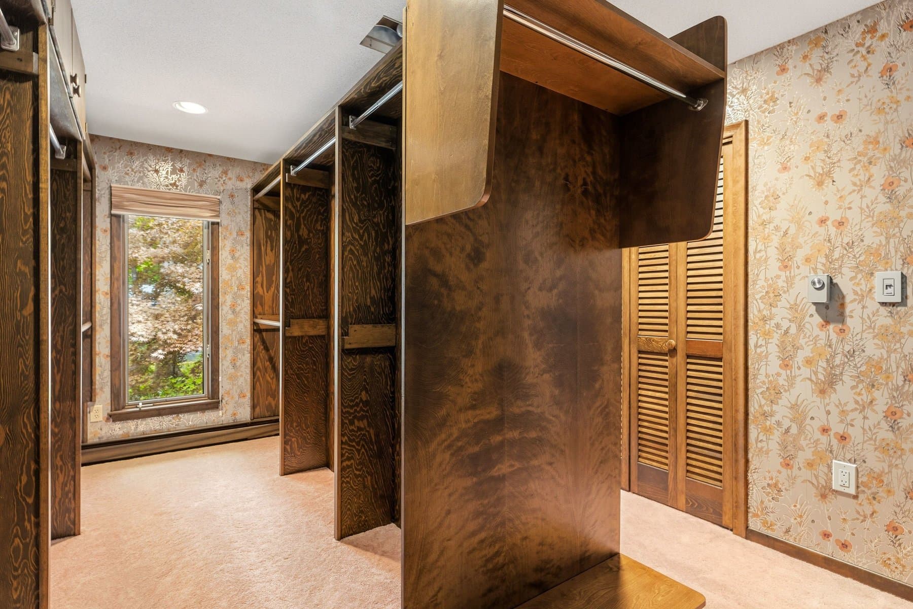 The dressing room off the primary bedroom, with hanging rods, built-in wood cabinets, and a window
