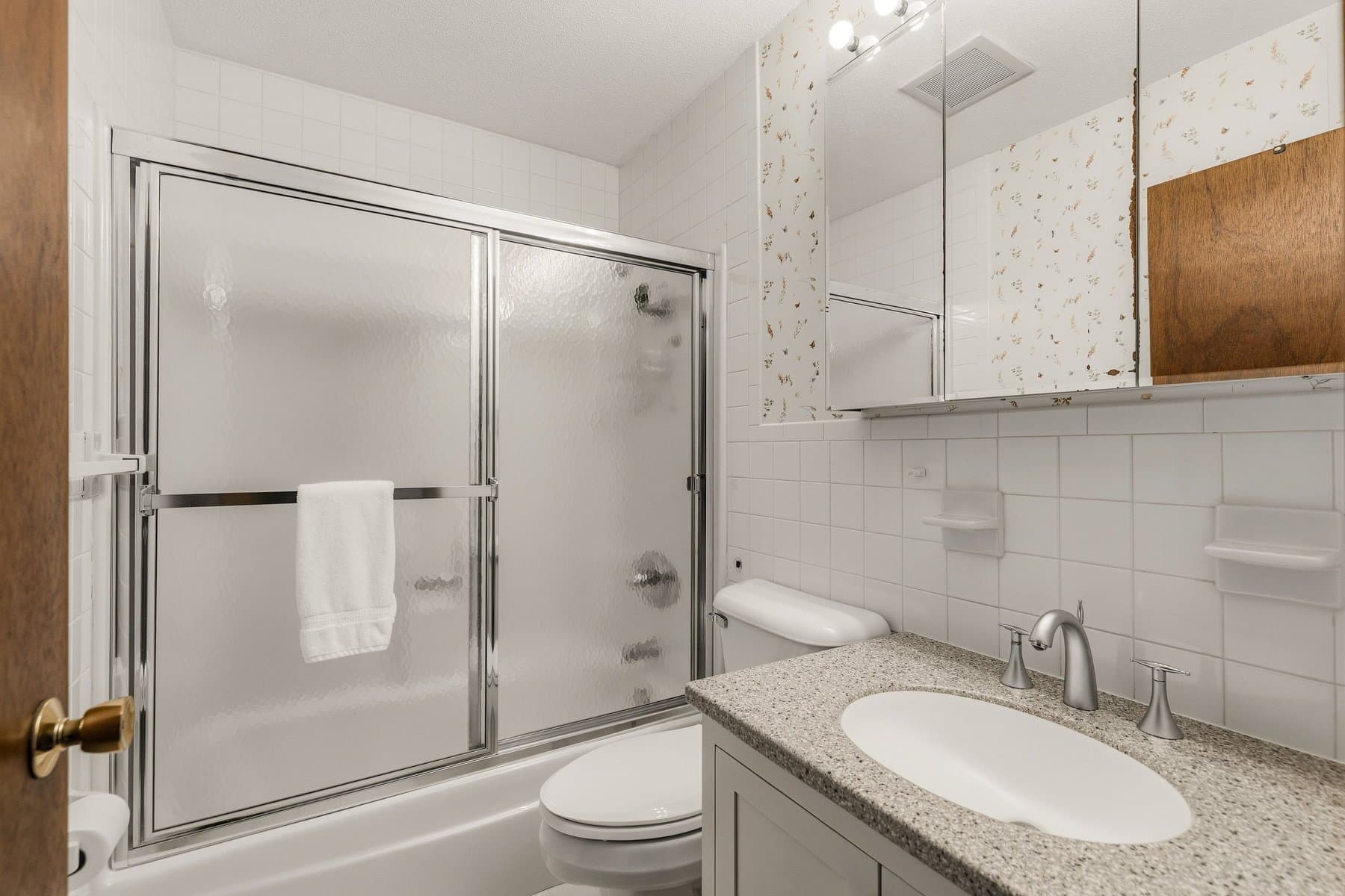 The hall bath with a tub and shower behind sliding glass doors and a granite vanity