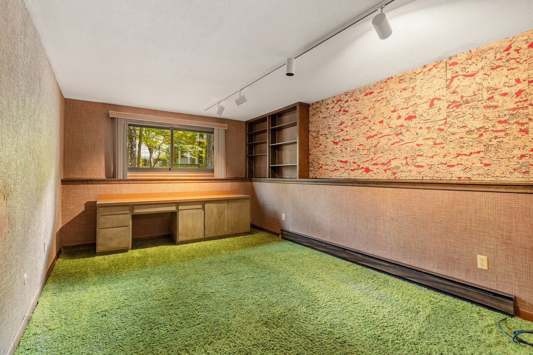 The lower-level bedroom with a built-in desk under the window, shelves, and green carpet