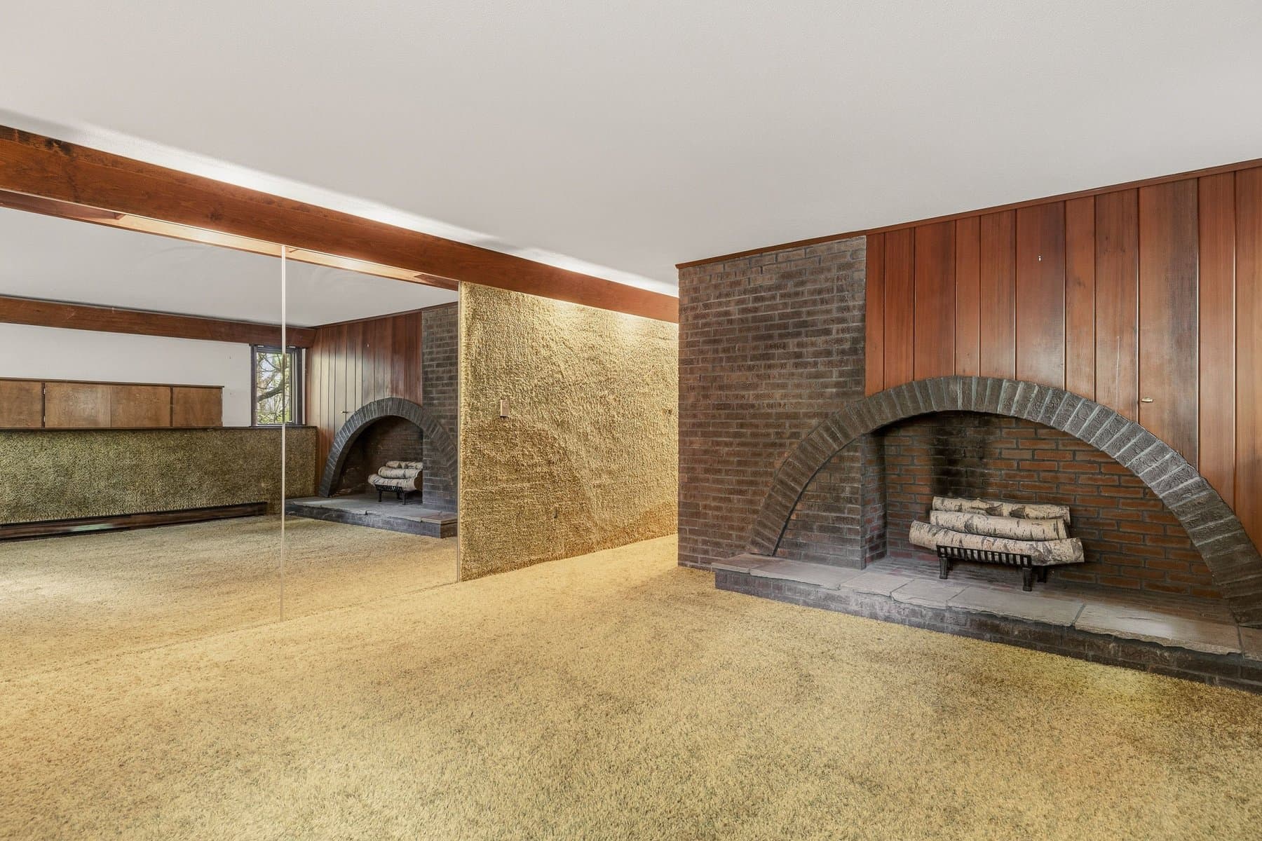 The rec room's mirrored wall reflecting the arched brick fireplace